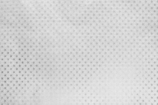 White background from metal foil paper with a pattern of sparkling stars closeup. Texture of silver metalized wrapping holiday paper surface.
