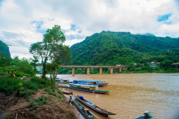 poblador local y barco con vistas sobre el río nam ou y las montañas de piedra caliza de la aldea de nong khiaw en laos - laos hut southeast asia shack fotografías e imágenes de stock