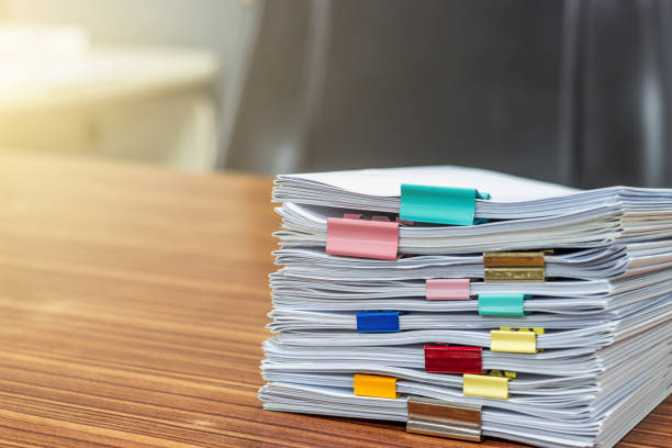 The stack of documents is arranged on the desk by sorting the job with a clip of colored paper. The stack of documents is arranged on the desk by sorting the job with a clip of colored paper. paper clip office supply stack heap stock pictures, royalty-free photos & images