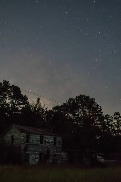The Milky Way rising above East Texas pines with an old house in the foreground.