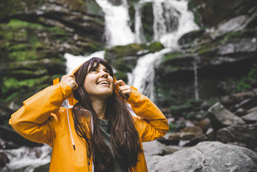 smiling woman in yellow raincoat with waterfall on background. hiking concept