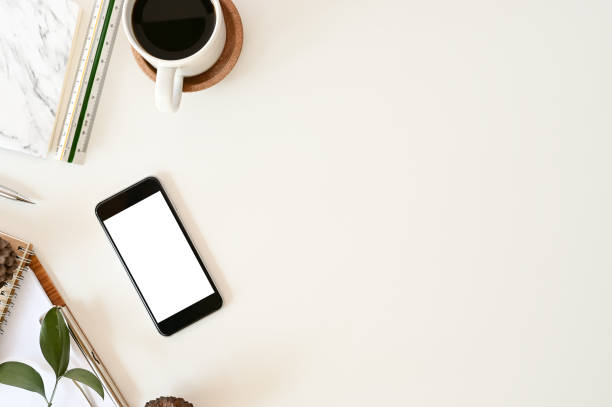 istock Top view office desk. Workspace with mockup smartphone, keyboard and office supplies, pencil, green leaf with coffee on white background. 1080103082