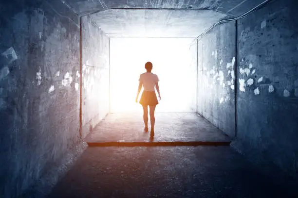 Photo of Woman walking through a dark tunnel