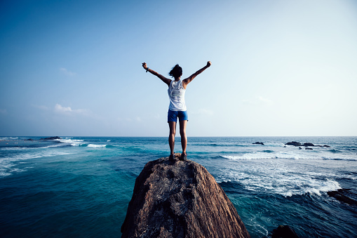 Freedom young woman outstretched arms on seaside rock cliff edge