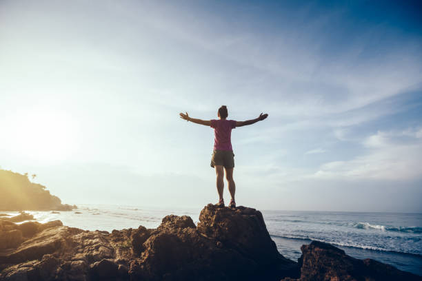 femme de liberté tendus bras sur le bord de falaise de lever de soleil station balnéaire rock - waters edge photos et images de collection