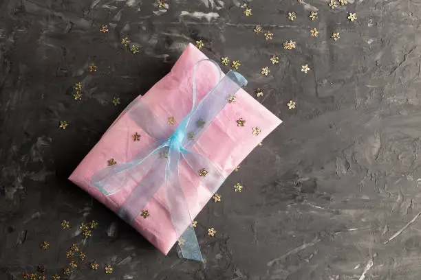 Pink gift box with blue tape lies on a dark concrete table. Top view. Copy space