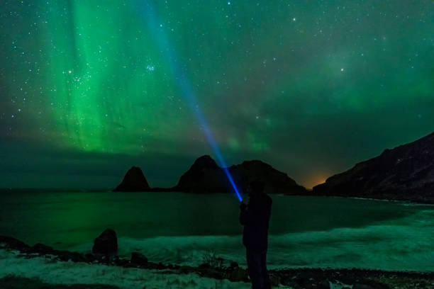 istock Man with a flashlight looking at Northern Lights, Aurora Borealis over the Lofoten 1080131774