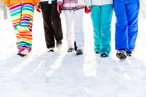 Low section of five friends walking along snowy field on winter holiday.