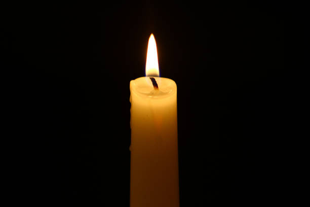 istock big paraffin lighting yellow candle with big flame on heavy black background. 1080143982