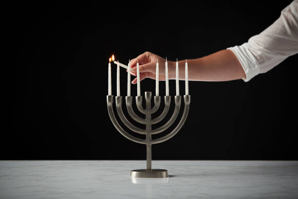 candela per l'illuminazione a mano su metallo hanukkah menorah su superficie in marmo su sfondo studio nero - hanukkah menorah human hand lighting equipment foto e immagini stock