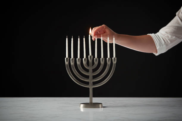 candela per l'illuminazione a mano su metallo hanukkah menorah su superficie in marmo su sfondo studio nero - hanukkah menorah human hand lighting equipment foto e immagini stock