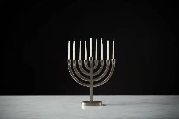 Photo of Metal Hanukkah Menorah With Unlit Candles On Marble Surface Against Black Studio Background