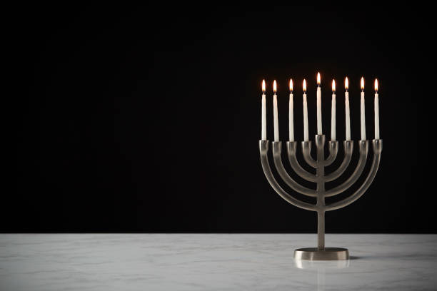 Lit Candles On Metal Hanukkah Menorah On Marble Surface Against Black Studio Background