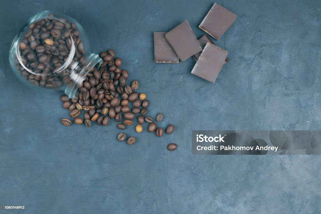 roasted coffee beans poured from a glass jar. angular placement of a coffee object with chocolate pieces. on dark concrete. view from above. copy space. roasted coffee beans poured from a glass jar. angular placement of the coffee object. Bag Stock Photo