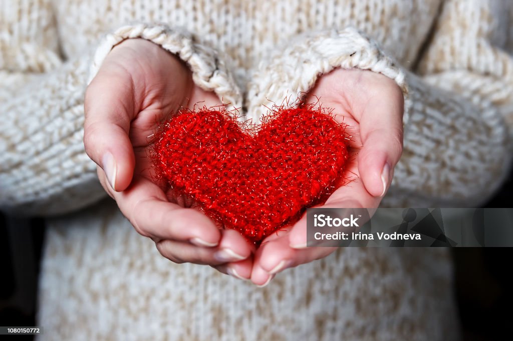 Girl in a light sweater gives a knitted heart. Girl in a light sweater gives a knitted heart. Close-up Vacations Stock Photo