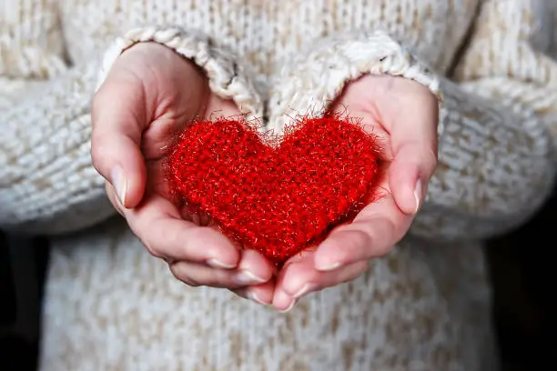 Photo of Girl in a light sweater gives a knitted heart.