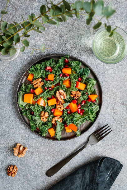 istock Top view on a vegan fresh salad which is made from raw vegetables such a persimmon, kale, pomegranate seeds and walnut on a grey background. Healthy food and lifestyle concept, flat lay. 1080158762