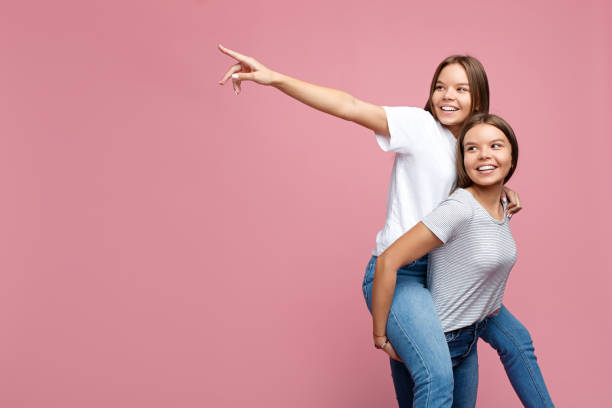 istock Handsome two young twin sisters with beautiful smile pointing finger away over pink background. Text space. 1080163636