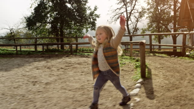 Little girl laughing and singing while walking across the horse pen at a sunny ranch