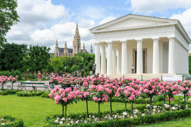 Tourists visiting the Theseus Temple in Volksgarten park with the City Hall at the background, Vienna, Austria