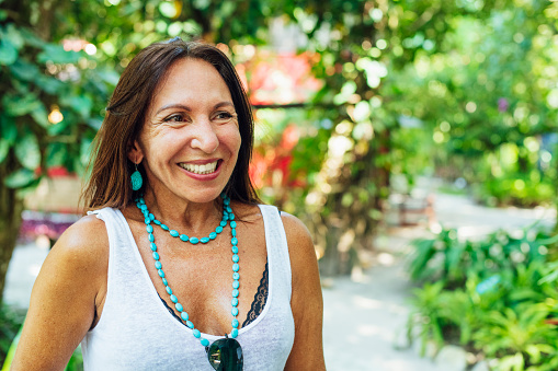 Portrait of attractive senior Brazilian woman smiling, wearing turquoise necklace and earrings, looking away