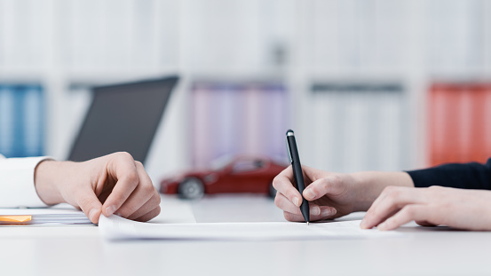 Woman signing a car insurance in the office, model car on the background