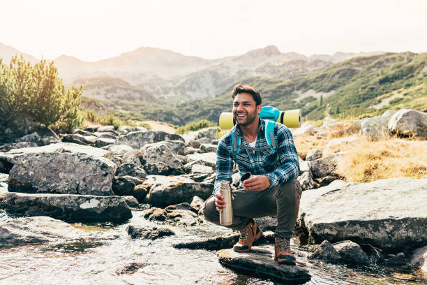 feliz caminhante por um riacho de montanha - men on top of climbing mountain - fotografias e filmes do acervo