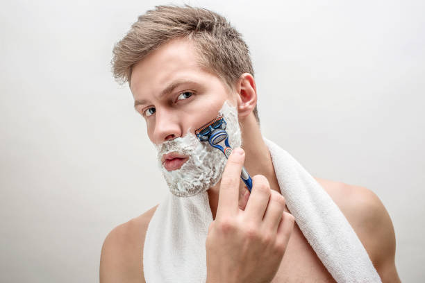 Portrait of young man shaving. He has white foam on beard. Guy is serious and concentrated. Isolated on white background. Portrait of young man shaving. He has white foam on beard. Guy is serious and concentrated. Isolated on white background shaving stock pictures, royalty-free photos & images