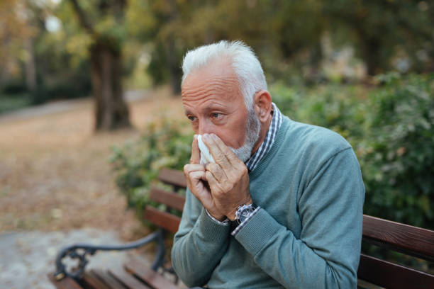 istock Elderly man with cold blowing his nose in the park 1080208894