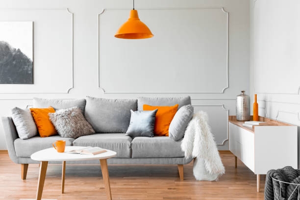 istock Orange lamp above table and grey settee with cushions in bright flat interior with poster. Real photo 1080213784