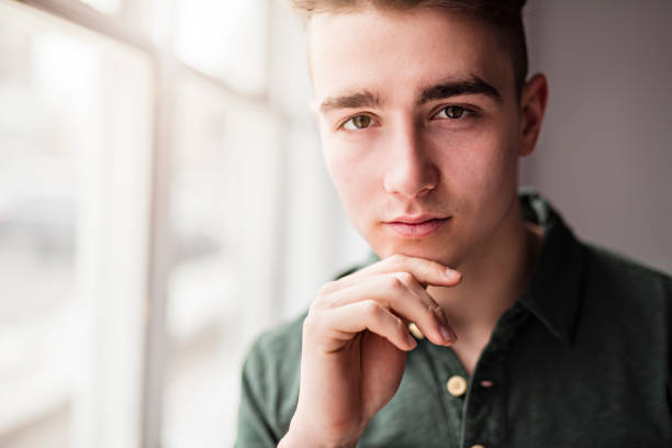 Portrait of a happy young man in his bedroom, with bookshelf behind.