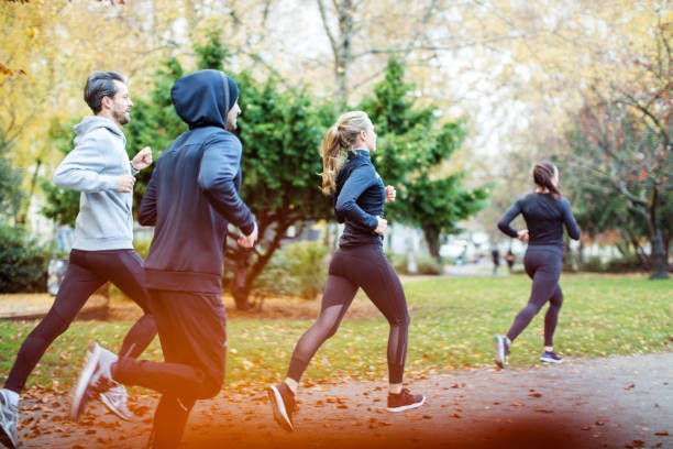 Small group of people running in the autumn park Small group of people running in the park in the autumn. Young people dressed in sportswear jogging together in morning. running motion stock pictures, royalty-free photos & images