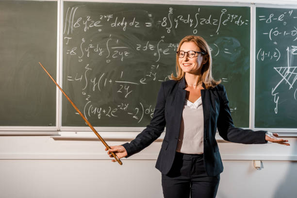istock smiling female teacher with wooden pointer explaining mathematical equations in classroom 1080232482