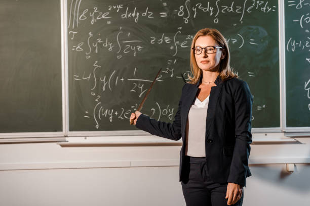 istock beautiful female teacher with wooden pointer explaining mathematical equations in classroom 1080232506