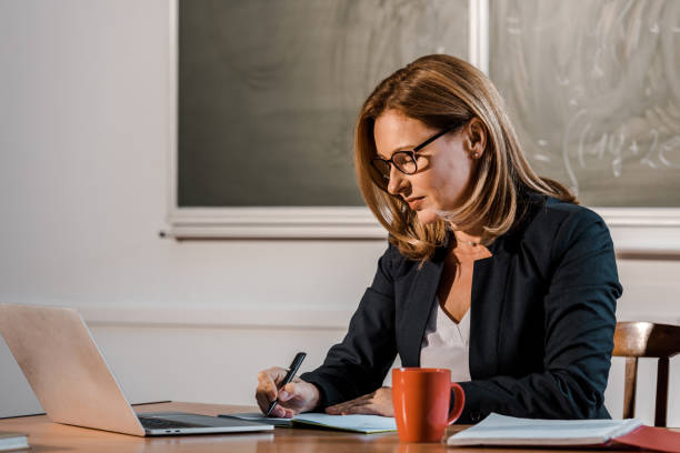 istock female teacher sitting at computer desk and writing in notebook during lesson in classroom 1080232548