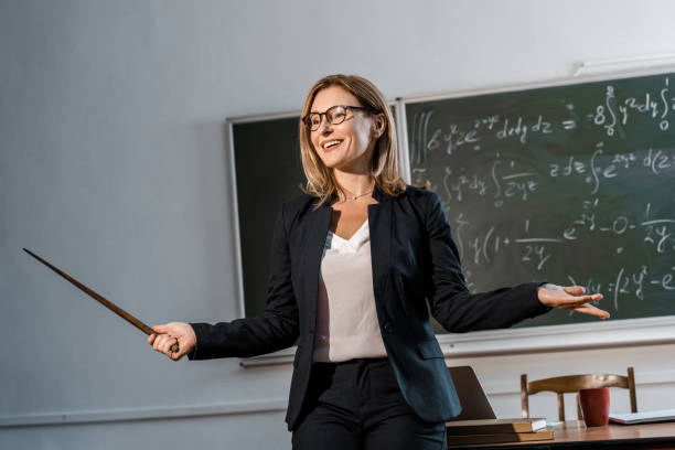 istock smiling female teacher with wooden pointer explaining mathematical equations in classroom 1080232570