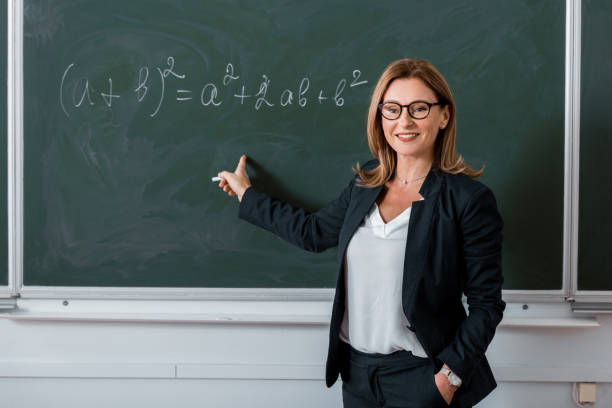 female teacher pointing with finger at mathematical equation on chalkboard in class female teacher pointing with finger at mathematical equation on chalkboard in class math teacher stock pictures, royalty-free photos & images