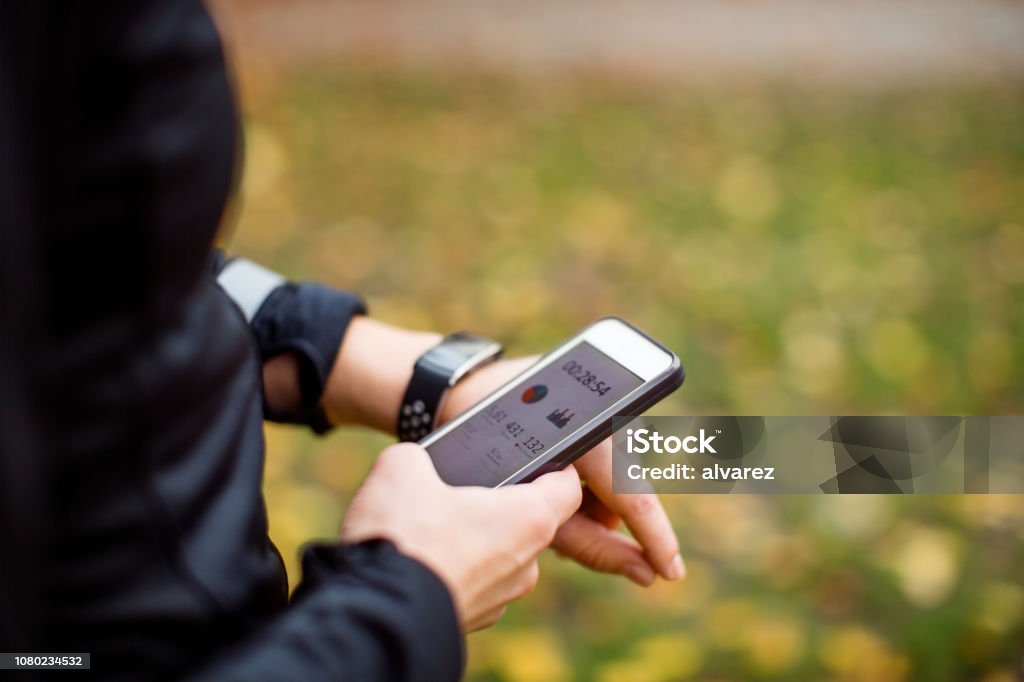 Woman using tech during fitness workout Close up of a urban runner using sporty smart watch and smartphone app for training. Jogger syncing her smart watch with smartphone during training outdoors. Healthy Lifestyle Stock Photo