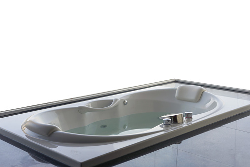 Empty white massaging jetted bathtub with large open window and sea view background.