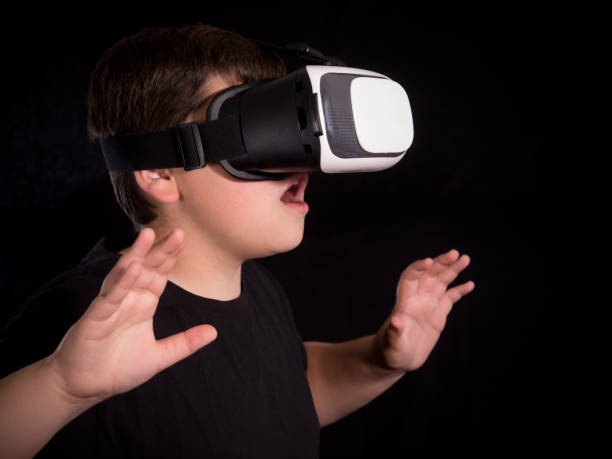 istock Boy wearing a virtual reality glasses surprised by what he is seeing in the simulation or game, isolated on black background 1080236216