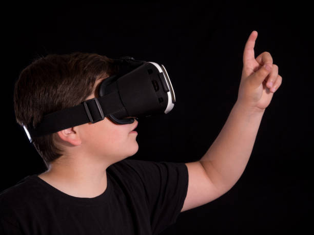 istock boy wearing a virtual reality glasses pointing with his finger something he is watching in simulation or game, isolated on black background 1080236392