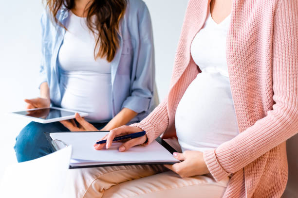 istock pregnant women using digital tablet and writing in forms during prenatal class isolated on grey 1080236672