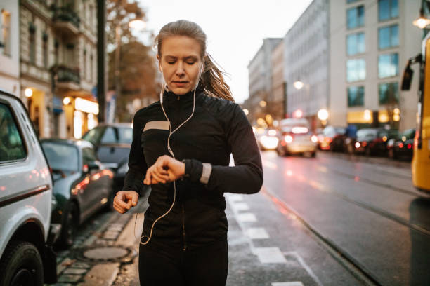 Urban runner checking heart rate on smartwatch Young woman running in the city and looking at her wristwatch. Female runner checking heart rate on smartwatch while running. taking pulse stock pictures, royalty-free photos & images