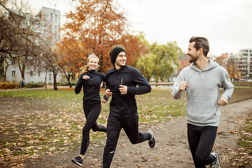 Small group of people running in park in autumn. Young men and woman jogging in the park together.