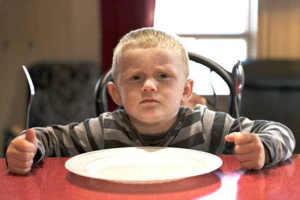 Upset little boy waiting for dinner while holding a fork and a spoon