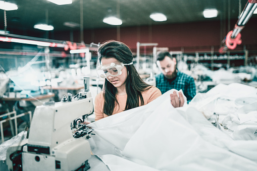 Young Female Textile Worker With Protective Eyewear Sewing Sheets On Sewing Machine