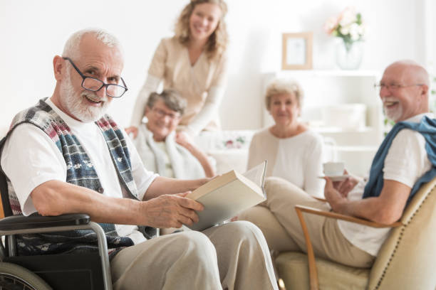 istock Old man with glasses sitting on wheelchair reading a book 1080278260