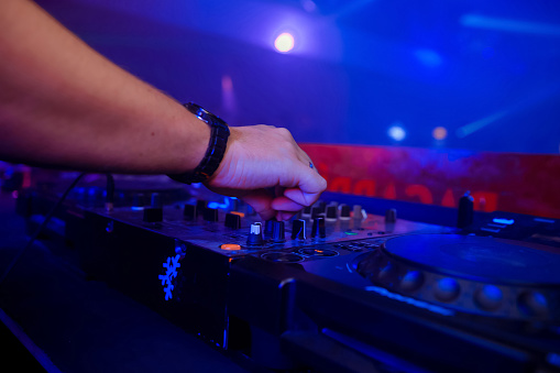 control DJ for mixing music with blurred people dancing at party in nightclub