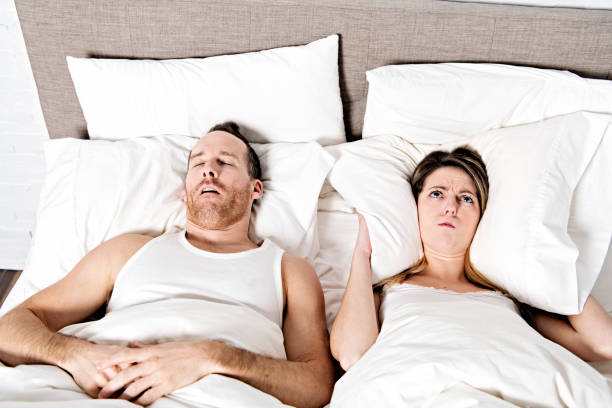 女性は、男がベッドの上でいびきしながら耳をブロック - sleeping lying on back couple bed ストックフォトと画像