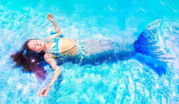 Above view of beautiful girl in mermaid costume floating in swimming pool with eyes closed